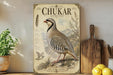 a vintage-style poster of a chukar, a type of bird, displayed on a wall next to a wooden cutting board and some kitchen utensils.