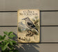 A metal sign with a detailed illustration of a bird, labeled as " Clark's Nutcracker", is mounted on a wall next to a plant.