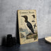 a metal plate with an illustration of a Common Murre, a type of sea bird, standing on a rock with a coastal landscape in the background.