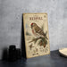 a vintage-style metal sign with a bird illustration, placed on a table next to some black camera lenses.