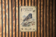 a vintage-style metal sign with a bird illustration, mounted on a wooden wall.
