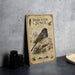 a vintage-style metal sign with illustrations and text, placed on a table next to some black camera lenses.