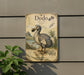 a vintage-style illustration of a dodo bird, which is a flightless bird native to the island of Mauritius. The dodo is depicted in a detailed and ornate illustration, showcasing its unique features and characteristics. The illustration is mounted on a wall, and there is a plant visible in the foreground.