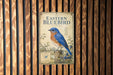 a vintage-style poster of a bluebird, mounted on a wooden wall.