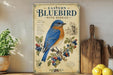 a vintage-style sign with a bluebird illustration, surrounded by various kitchen items such as a cutting board, lemons, and a potted plant.