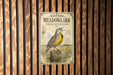 a vintage-style sign for Eastern Meadowlark singing on a fencepost, with a detailed illustration of a yellow and black bird perched on a wooden post.