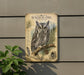 a detailed illustration of a Screech- Owl, a species of owl known for its distinctive appearance and habitat. The owl is perched on a branch, surrounded by pine needles and pine cones, creating a natural and serene setting. The image is mounted on a wall, and there is a plant visible in the foreground, adding a touch of greenery to the scene.