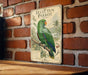 A vintage-style metal plaque featuring an illustration of a green parrot, mounted on a brick wall.