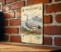 A metal plaque featuring an illustration of an Emperor Goose standing on a grassy area with mountains in the background.