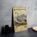 A framed illustration of an Emperor Goose standing on a grassy area with mountains in the background.