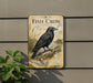 a vintage-style metal sign with a black bird, likely a crow, perched on a branch. The sign is mounted on a wall and is surrounded by greenery, including a plant.