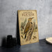 a wooden plaque with an illustration of a gilded flicker bird perched on a tree branch, surrounded by pine cones and pine needles.