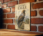 a vintage-style metal sign with an illustration of a golden eagle perched on a rocky outcrop, mounted on a brick wall.