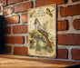 A vintage-style metal sign with illustrations and text about the Great Crested Flycatcher, mounted on a brick wall.