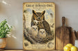 A framed poster of a great horned owl with its young nestled in a tree, accompanied by text and illustrations, is displayed on a shelf next to a wooden cutting board and a potted plant.