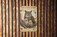 A poster of a great horned owl with its young nestled in a tree, displayed on a wooden wall.