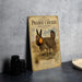 A vintage-style metal sign with illustrations of a prairie chicken and a field of grass, along with text, is displayed on a gray concrete surface.