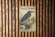 A vintage-style poster of a heron, featuring a detailed illustration of the bird and its natural habitat, is displayed on a wooden wall.