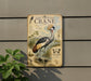 a grey and white bird, possibly a crane, standing in a natural setting with plants and water.