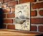 a vintage-style metal plaque with a detailed illustration of a gull-billed tern, mounted on a brick wall.