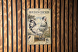 A poster of a Houdan chicken is displayed on a wooden wall.