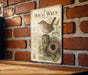 a sign with a picture of a bird, specifically a house wren, perched on a branch and nestled in a nest. The sign is mounted on a brick wall, and there is a wooden table below it.