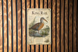 A metal sign with an illustration of a bird, likely a king rail, is mounted on a wooden wall.