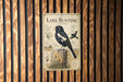 a vintage-style metal sign with an illustration of a black and white bird, likely a lark bunting, perched on a wooden post.