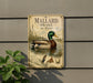 A metal sign with a duck illustration and text, mounted on a wall next to a plant.