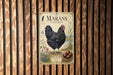 a vintage-style metal sign with a black rooster and brown eggs, mounted on a wooden wall.