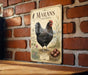 A vintage-style metal sign featuring a black chicken standing on a straw-covered ground, with illustrations of plants and eggs, mounted on a brick wall.