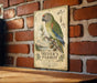 A vintage-style metal sign featuring a colorful parrot perched on a branch, mounted on a brick wall.
