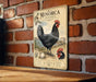 a vintage-style metal sign with a black chicken illustration, mounted on a brick wall.