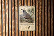 a metal plaque with an illustration of a quail bird, mounted on a wooden wall.