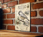 A metal sign with a bird illustration and text is mounted on a brick wall.