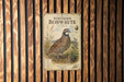 a vintage-style illustration of a Northern Bobwhite bird, which is a type of bird of prey, standing on a grassy field with some berries nearby.