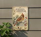 A vintage-style sign featuring a red cardinal bird perched on a branch with pine needles and berries, mounted on a gray wall.