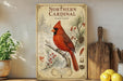 A vintage-style poster of a red cardinal perched on a branch, surrounded by pine cones and berries, is displayed on a shelf next to a wooden cutting board and a potted plant.