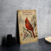 A vintage-style metal sign with a red cardinal perched on a branch, surrounded by pine cones and berries, is displayed on a gray countertop.