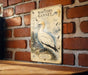 a vintage-style illustration of a Northern Gannet bird, which is a type of sea bird, mounted on a brick wall.