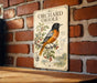 A vintage-style metal sign featuring an illustration of an orange and black oriole bird perched on a branch with berries, mounted on a brick wall.