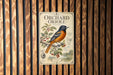 A vintage-style metal sign featuring an illustration of an oriole bird perched on a branch with berries, against a wooden background.