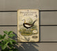 A vintage-style metal sign with illustrations of a bird and aquatic plants, mounted on a wall next to a plant.