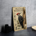 A framed illustration of a woodpecker is displayed on a table, accompanied by a stack of black camera lenses and a woven basket.
