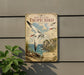 a vintage-style metal sign with a tropical bird illustration, mounted on a wall next to a plant.