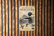 A metal sign with a picture of a red-breasted merganser duck, mounted on a wooden wall.