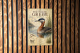 a vintage-style metal sign with a red-necked grebe, a type of water bird, depicted in a lake setting.