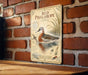 A vintage-style metal sign featuring an illustration of a red phalarope bird, mounted on a brick wall.