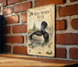 A vintage-style metal sign featuring an illustration of a ring-necked duck, mounted on a brick wall.