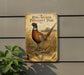 A metal sign with an illustration of two pheasants, one with a ring-nacked appearance and the other with a plain plumage, mounted on a wall.